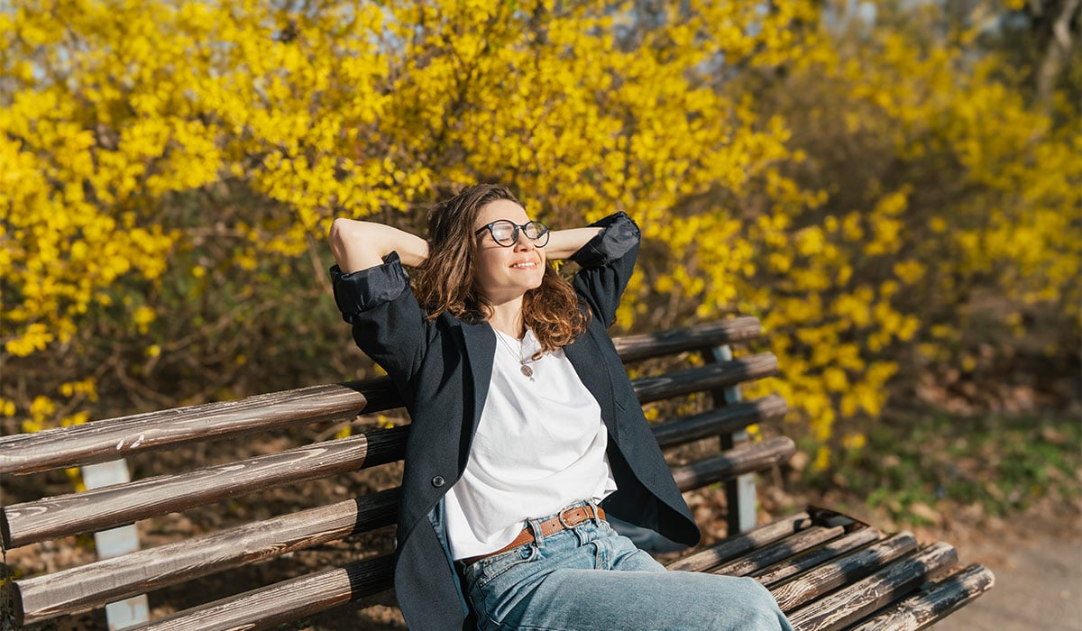 Relaxed young curly woman in glasses enjoying spring sun on a city bench; Shutterstock ID 2755445191; purchase_order: -; job: -; client: -; other: