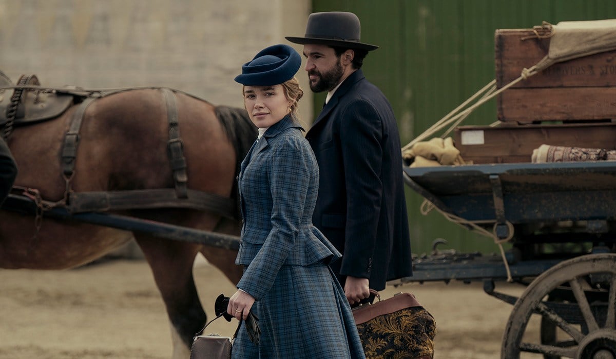 October "A woman and man in period clothing walk beside a horse-drawn wagon loaded with luggage and crates, set in a rustic outdoor location, evoking a historical setting."
