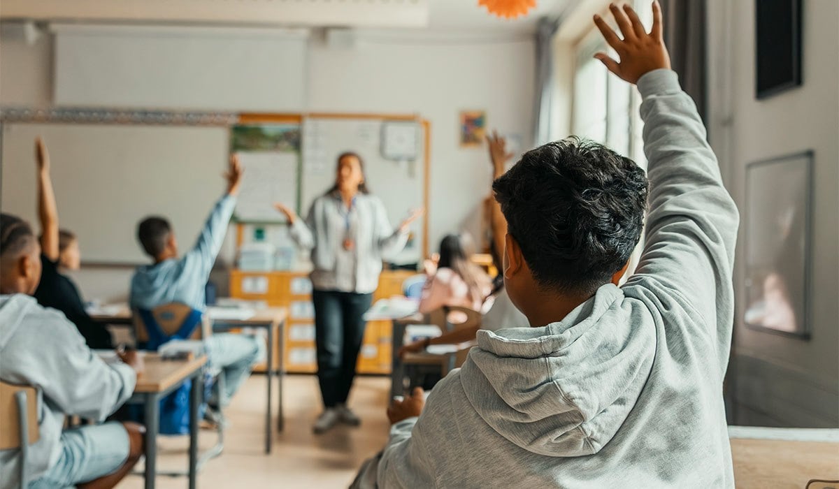 Rear view of boy raising hand during Q and A session in classroom at elementary school